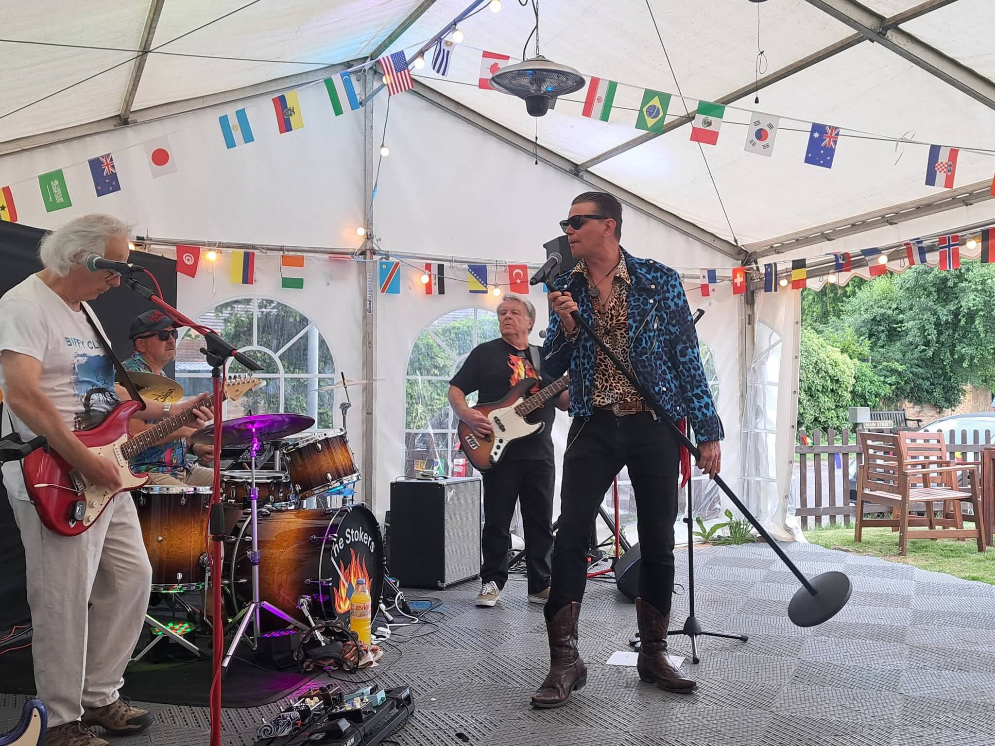 A band playing on a small stage in the marquee, with guitarists and a singer under coloured lights